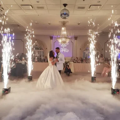 A newlywed couple dances on a cloud of fog, surrounded by sparklers in a decorated venue.