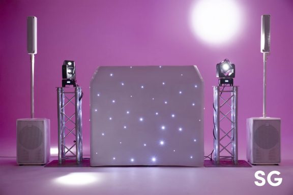 A DJ setup with illuminated speakers and a sparkling backdrop on a pink stage.